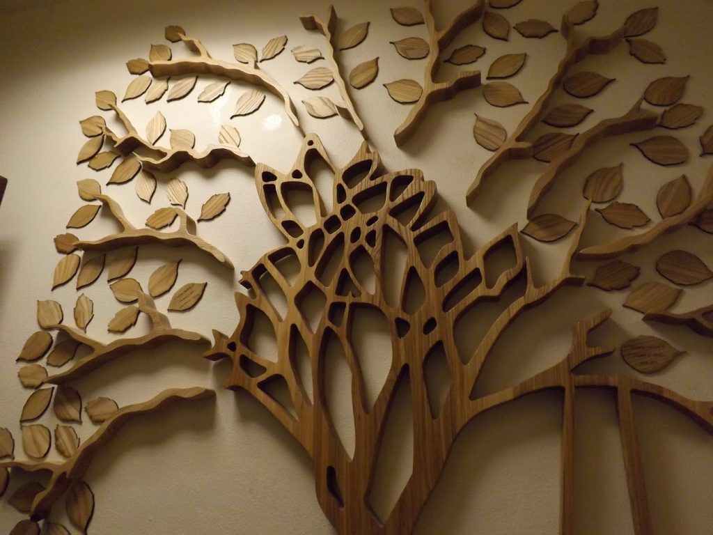 Wooden wall art depicting a stylized tree with branches and leaves mounted on a light-colored wall.