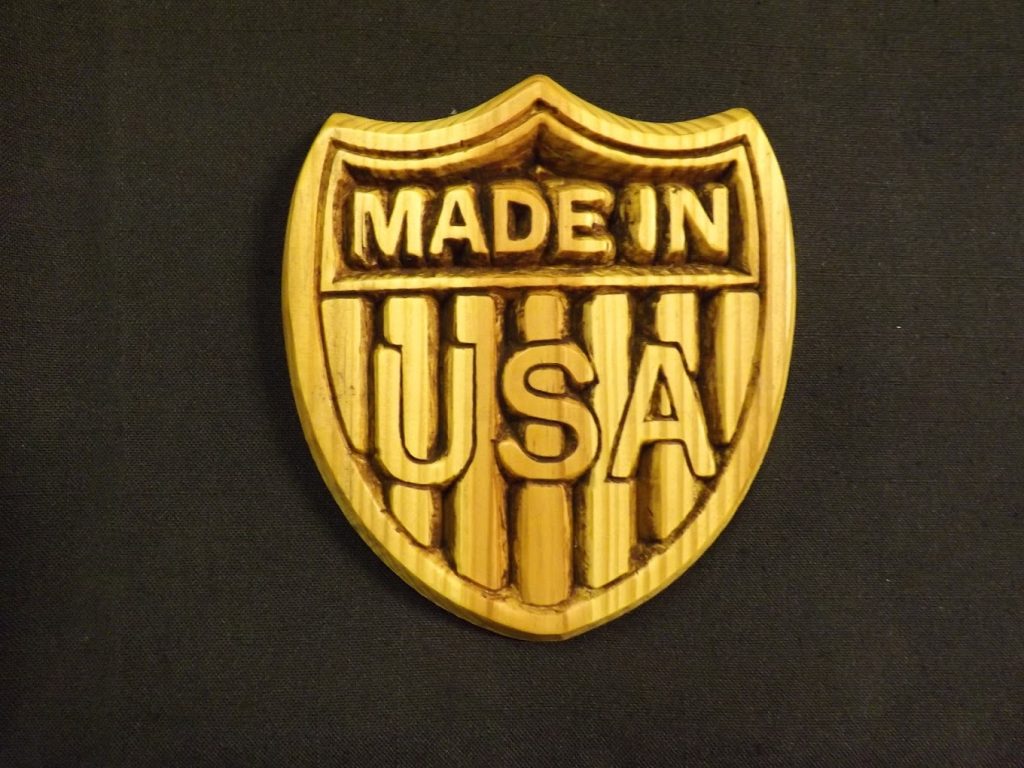 Wooden shield-shaped plaque with "Made in USA" engraved on it, set against a plain black background.