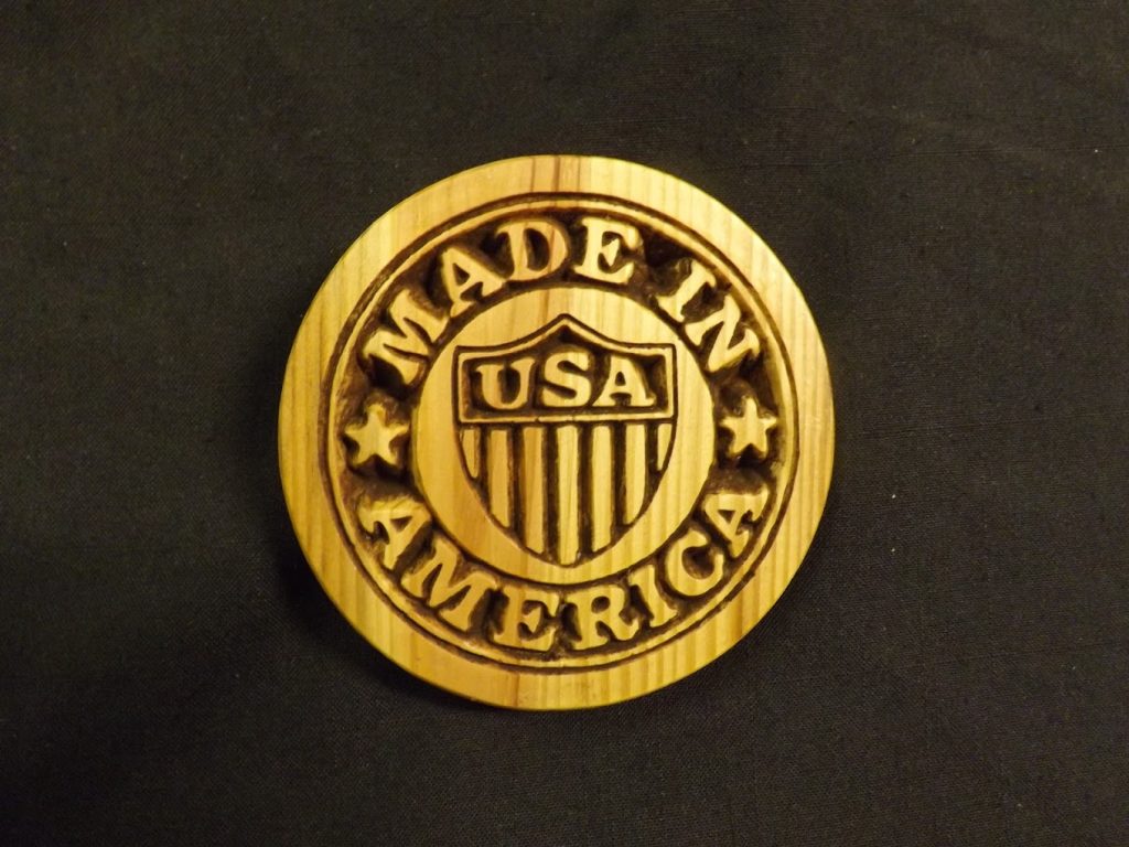A round wooden plaque with "MADE IN AMERICA" and "USA" carved in the center on a black background.