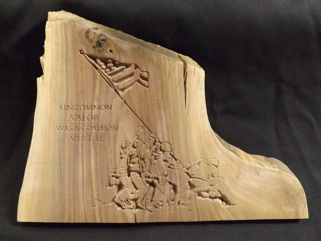 Wood carving of soldiers raising a flag with the words "Uncommon valor was a common virtue" engraved beside them.