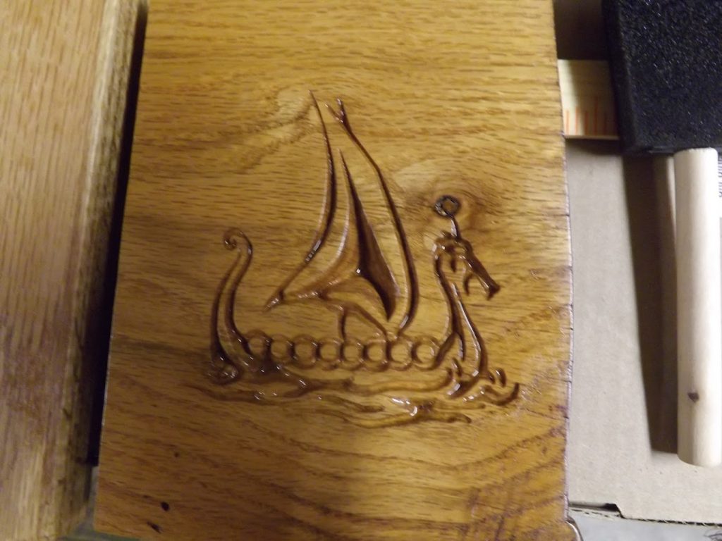 A carved Viking ship with a sail and dragon head is depicted on a polished wooden surface.